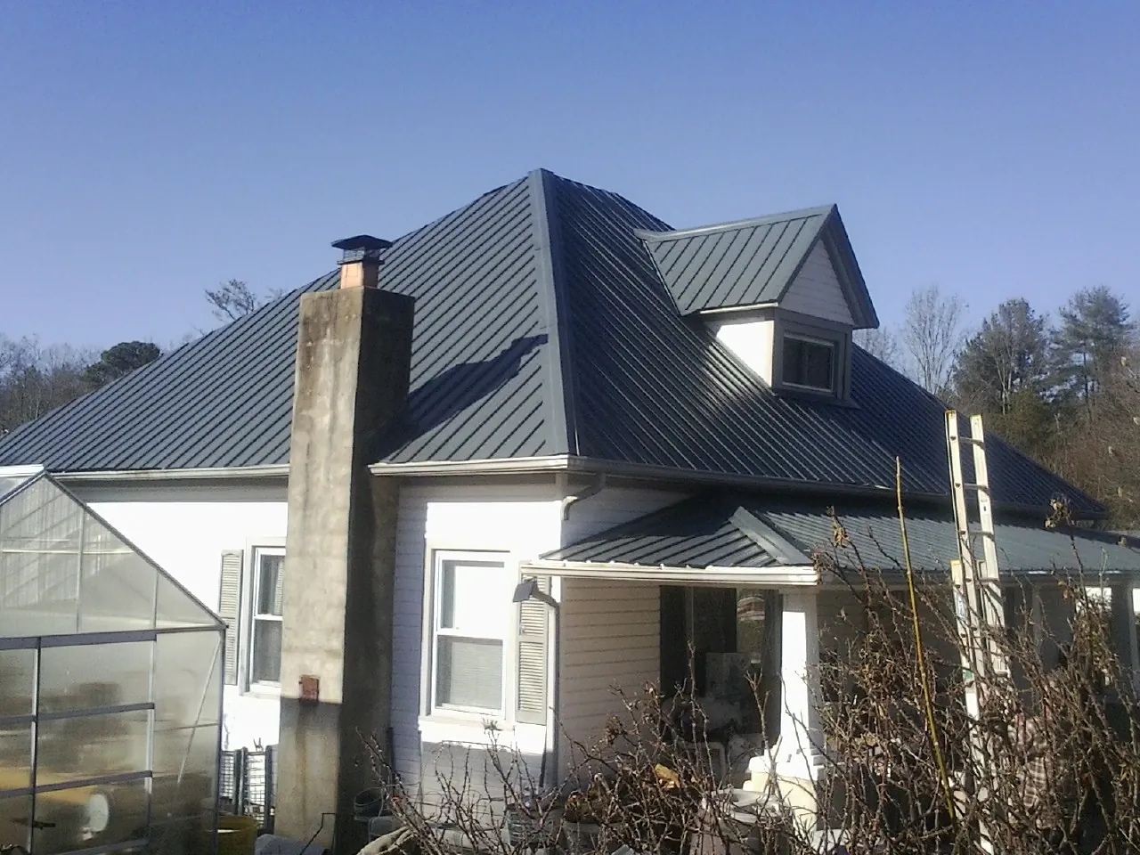 Dark blue standing seam metal roof on a white farmhouse with dormer — Slate & Tile Roof Repair by Roofing Brothers in Lutz