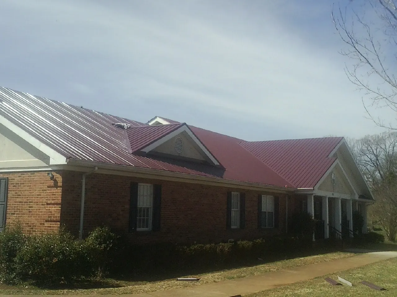 Red metal roof with gabled entries on a long brick building, from a Hail Damage Roof Repair job in Lutz