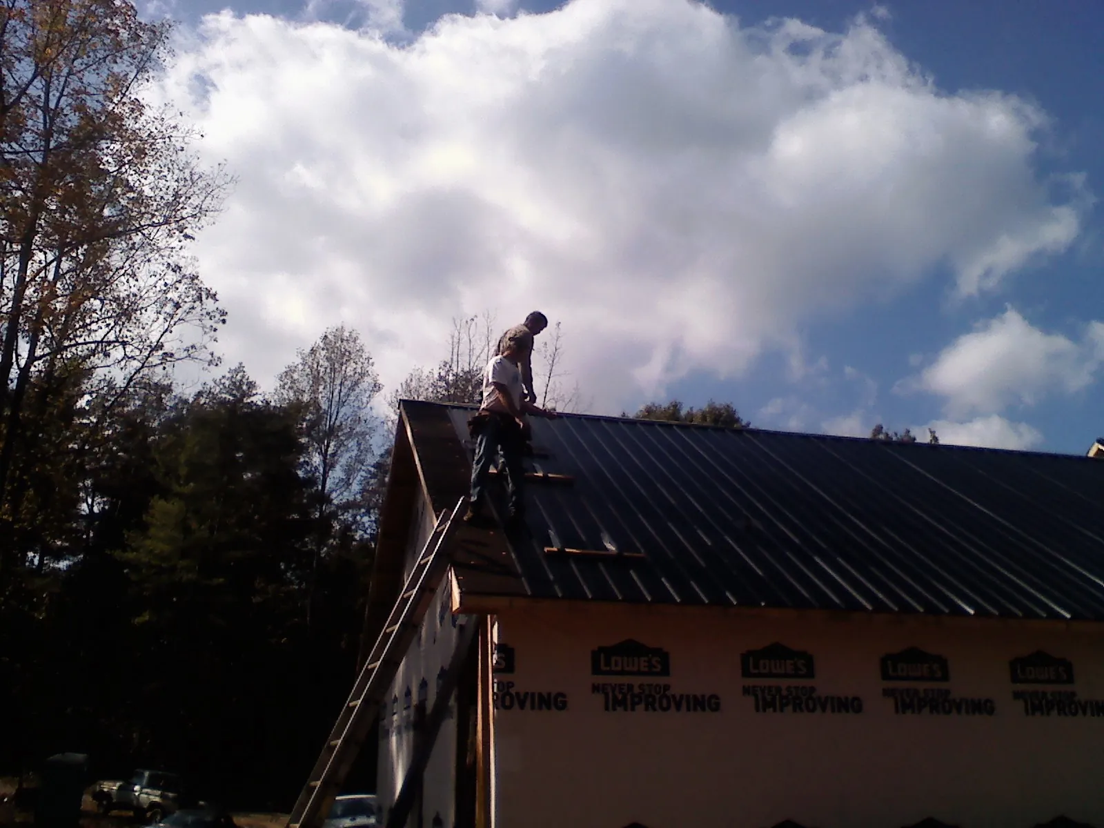 Roofer fastening dark metal panels high against a cloudy sky, from a Roof Inspection job in Lutz
